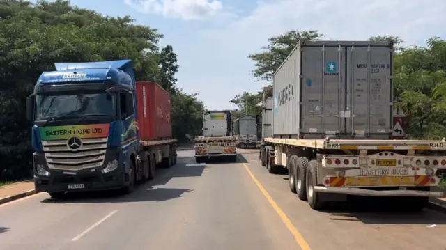 Amakamyo ane ari mu muhanda munini wa kaburimbo, atatu areba mu cyerekezo kimwe, naho indi kamyo ireba mu kindi cyerekezo.