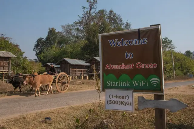 လမ်းဘေးက စတားလင့်ခ် အင်တာနက်ဆိုင် ဆိုင်းဘုတ်နဲ့ လမ်းမ‌ပေါ်က မောင်းနှင်သွားတဲ့ နွားလှည်းတစ်စီး