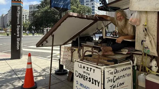Beskućnik sa dugom bradom i belom kosom sedi na stvarima na ulicama Vašingtona
