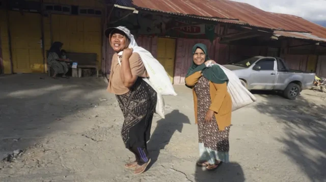 Potret dua orang perempuan di Kampung Bah, Kecamatan Ketol, Kabupaten Aceh Tengah saat memanggul bantuan dari pemerintah desa sat banjir besar akhir 2025.