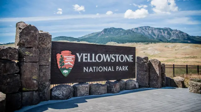 Placa de identificação do Parque Nacional de Yellowstone, nos Estados Unidos, com deserto e montanha ao fundo