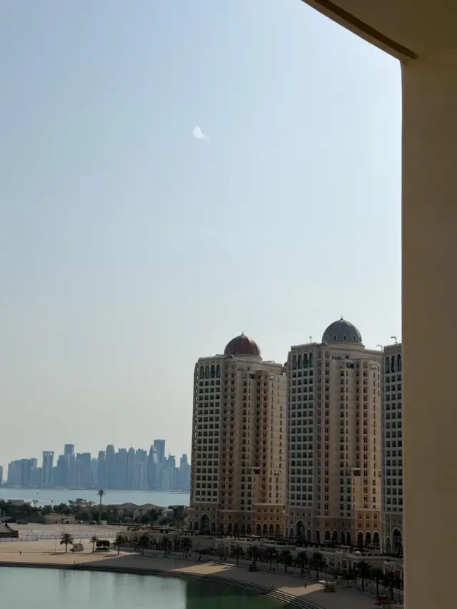 Una ciudad al fondo, edificios al frente y en el cielo despejado se ve una nube de humo blanco, señal de un misil derribado