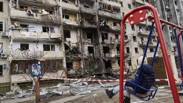 طفل يجلس على أرجوحة أمام مبنى سكني في كييف تعرض لأضرار جراء القصف الصاروخي في 25 فبراير/شباط عام 2022