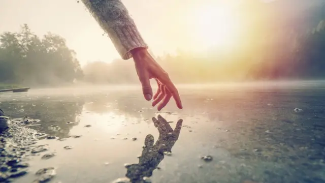 Una mano toca el agua de un lago.