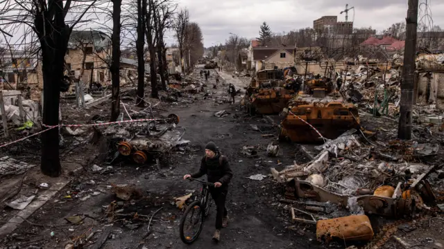 Un hombre empuja su bicicleta a través de escombros y vehículos militares rusos destruidos en una calle de Bucha, Ucrania.