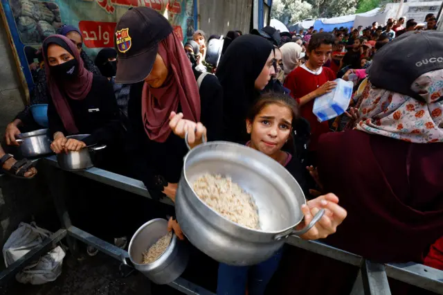 طفلة تحمل وعاءً وتنظر إلى الكاميرا وسط الزحام، تطلب طعاماً من مطبخ خيري في النصيرات وسط قطاع غزة، 28 سبتمبر 2025