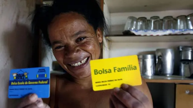 Una mujer muestra el carnet amarillo de Bolsa Familia mientras sonrie