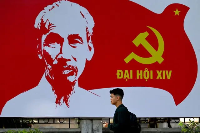 Một người đàn ông đi ngang qua áp phích quảng bá Đại hội Đảng Cộng sản Việt Nam lần thứ 14 với hình ảnh Chủ tịch Hồ Chí Minh, cờ Đảng, tại Hà Nội vào ngày 8/1/2026