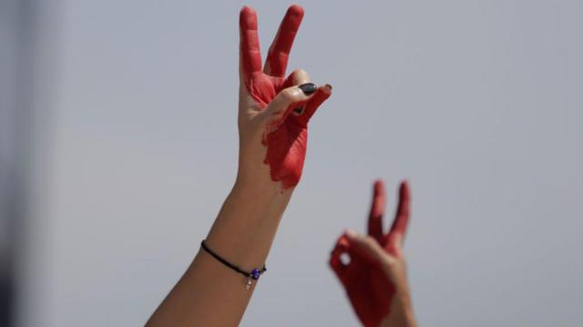 دست دو زن که به انگشتان قرمز رنگ‌شان را به نشانه پیروزی بالا برده اند