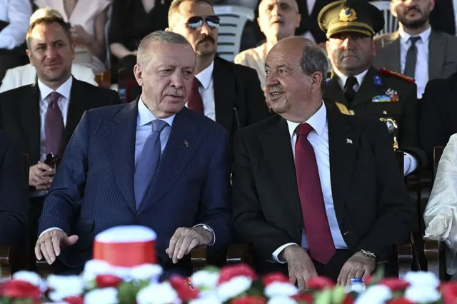 Erdoğan ve Tatar yan yana oturuyor. Konuşurlarken tebessüm ediyorlar.