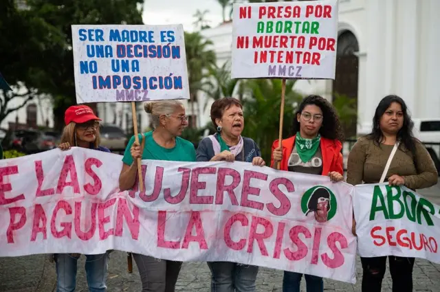 Mujeres con pancartas, una de ellas dice: "Ni presa por abortar, ni muerta por intentar"