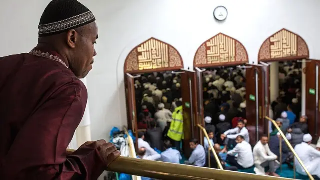 man looking from balcony at praying people in mosque