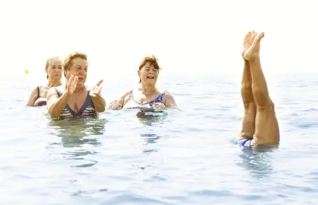 Un grupo de mujeres se divierten en el agua. Una se para de manos.