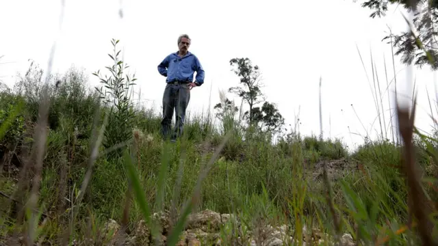 Hombre mira desde el borde de una fosa común.