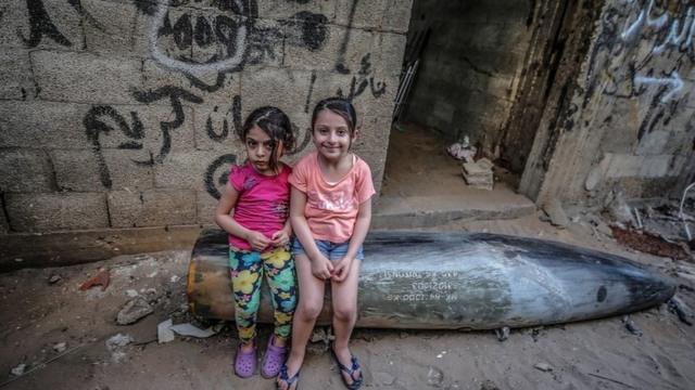 Irmãs palestinas sentam em um míssil não detonado disparado por aviões de guerra israelenses em Gaza