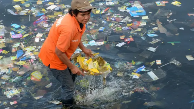 Imagem mostra mulher retirando plástico do oceano