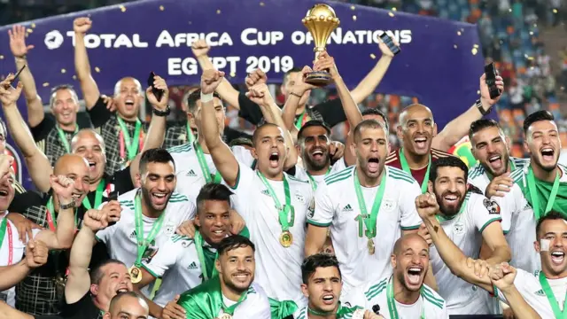 اللاعب رياض محرز يحمل كأس البطولة، وسط فريق الجزائر المحتفي بفوزه للمرة الثانية بكأس الأمم الأفريقية.