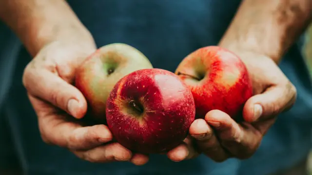 Manos unidas sosteniendo tres manzanas