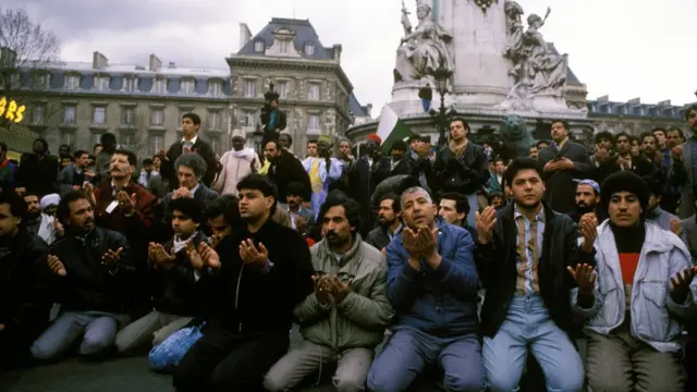 Homensbonus esportivopele morena clara e cabelos pretos se ajoelham com um prédio e uma estátua parisienses ao fundo