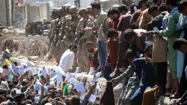 People crowd around soldiers, holding up their documents, outside Kabul airport, 26 August 2021.