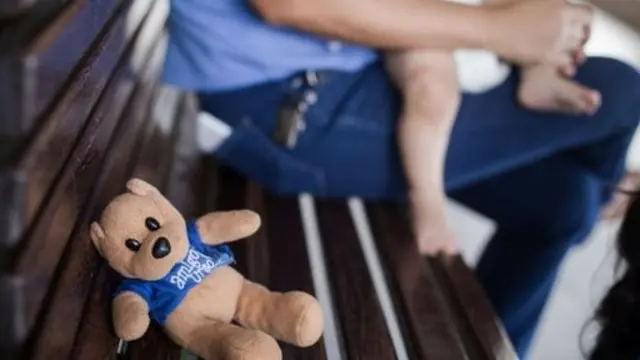 Osito en un banco y un bebé en la falda de un adulto en un hogar para niños en Fortaleza