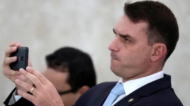 Flávio Bolsonaro segura celular, aparentemente filmando um evento