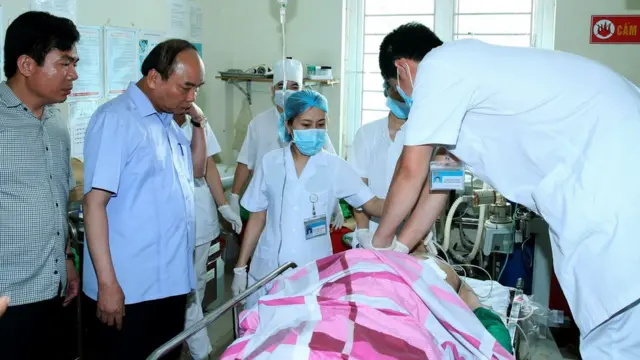 Vietnam's Prime Minister Nguyen Xuan Phuc (2L) looks at one of the victims of a shooting at a local hospital in the northern province of Yen Bai on August 18, 2016