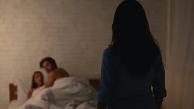 A woman looks at a man and a woman in bed