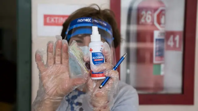 Una persona con mascarilla, alcohol y bolígrafo