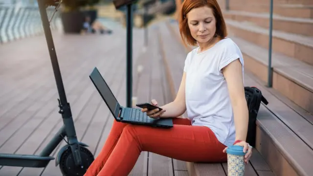 Une femme assise dans la rue avec son ordinateur portable débranché.