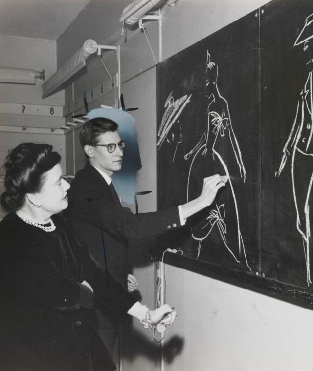 Yves Saint Laurent desenhando modelos no quadro-negro em 1957, ao lado de Madame Marguerite Carré, chefe das oficinas da Dior