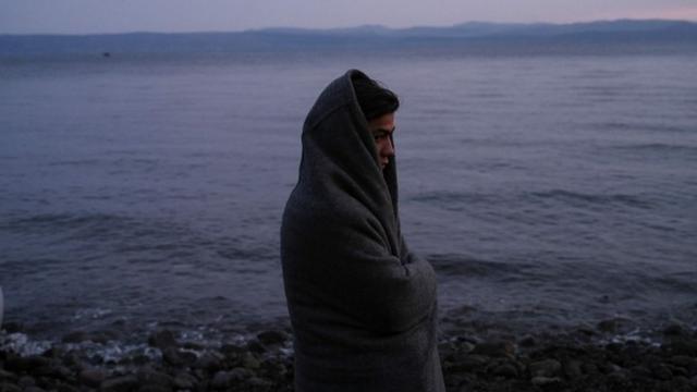 Женщина, закутавшаяся в одеяло, стоит на берегу моря на острове Лесбос