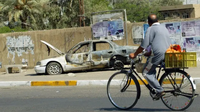 An Iraqi man rides a bicycle passing by a remains of a car burnt during a deadly incident involving Blackwater guards in Baghdad in September 2007
