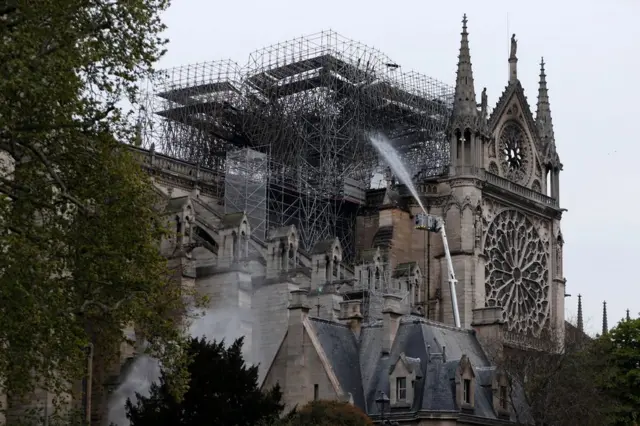 Firefighters spray water as they work to extinguish a fire at Notre-Dame Cathedral in Paris