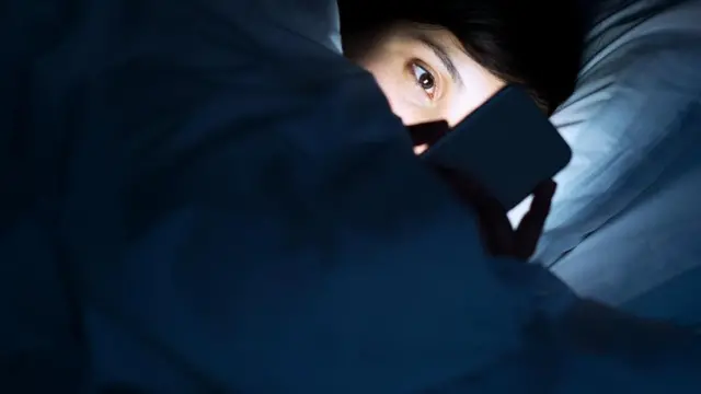 Una persona mirando su teléfono, en cama y en la oscuridad
