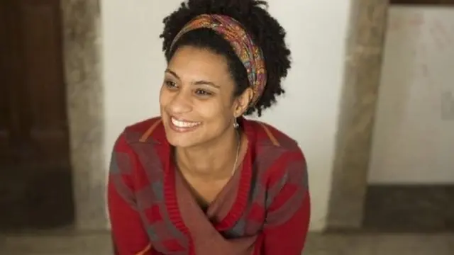 A vereadora Marielle Franco, uma mulher negra jovem e sorridente, com uma faixa nos cabelos crespos