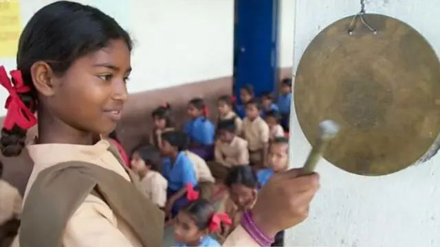 શાળાનો ઘંટ વગાડી રહેલી એક બાળકીની તસવીર