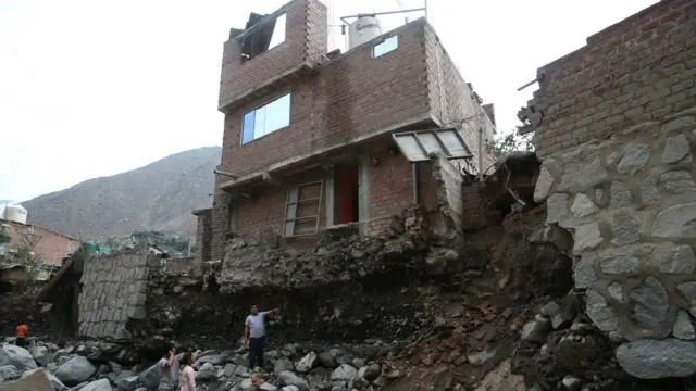 Hombre parado frente a una casa que parece a punto de caerse.