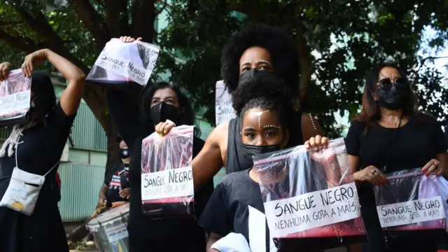 Mulheres seguram sacos plásticos com líquido vermelho e a frase "sangue negro, nenhuma gota a mais"