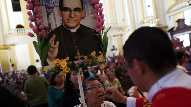 Una mujer recibe la comunión mientras carga una imagen de Monseñor Romero.