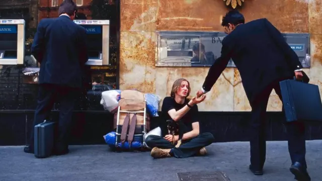 أحد الفقراء يجلس بجوار بنك ويطلب المساعدة المالية من المارة