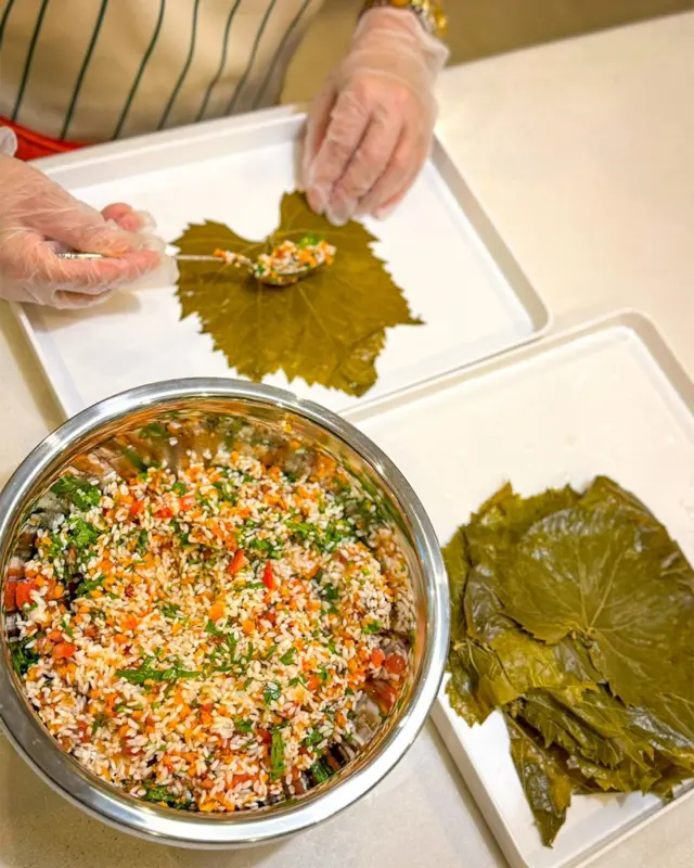 bir tenceredeki iç harcından alıp, üzüm yapraklarına dolma saran bir el. 