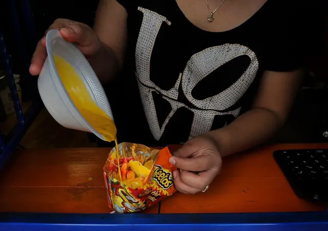 Mujer vertiendo una salsa de queso derretido sobre snacks de maíz.