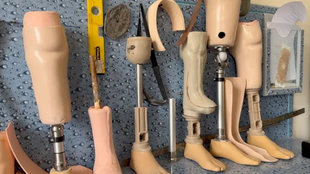  د مصنوعي پښو ګڼ ډولونه د یوه بل ترڅنګ اېښودل شوي چې دېوال ته ولاړ دي.
