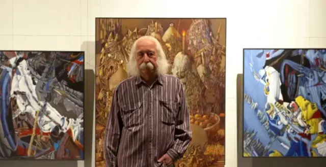 Марчук у картатій сорочці на фоні своїх картин 