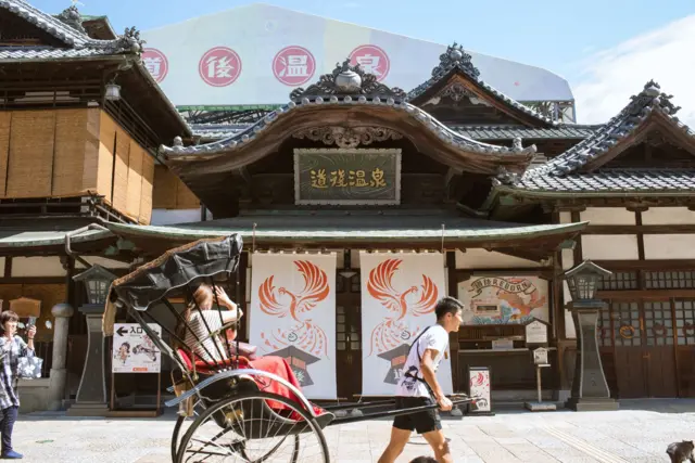 Turis menaiki becak di depan Dōgo Onsen Honkan.