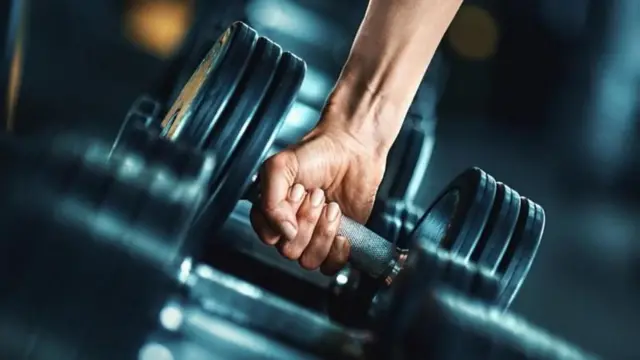 رجل يمسك بيده أوزاناً ثقيلة في صالة رياضية