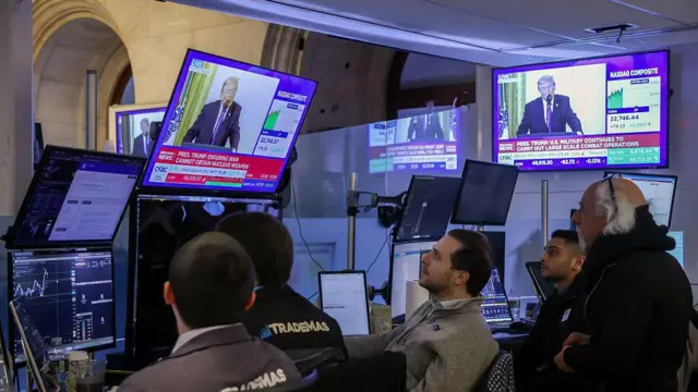 Bir televizyon kanalının Trump canlı yayını New York Borsası'nda (NYSE) canlı yayınlıyor. Bir ekranın önünde beş piyasa uzmanı oturmuş canlı yayını dinliyor.