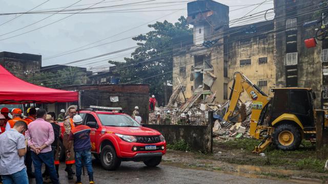 Imagem mostra bombeiros e retroescavadeirajogar xadrez on linefrente a prédio que desabou