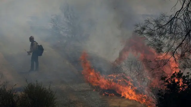 يسير أحد رجال الإطفاء التابعين لإدارة كال فاير بجوار ألسنة اللهب المتصاعدة من حريق 6-5 ضمن مجمع حرائق البرق في 3 سبتمبر/أيلول 2025 بالقرب من تشاينيز كامب، كاليفورنيا.